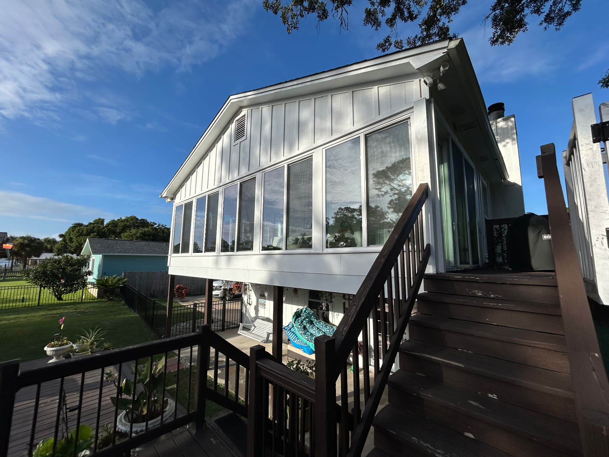 Exterior view of the white canal-front home from the backyard deck, showing the glass-walled Florida room