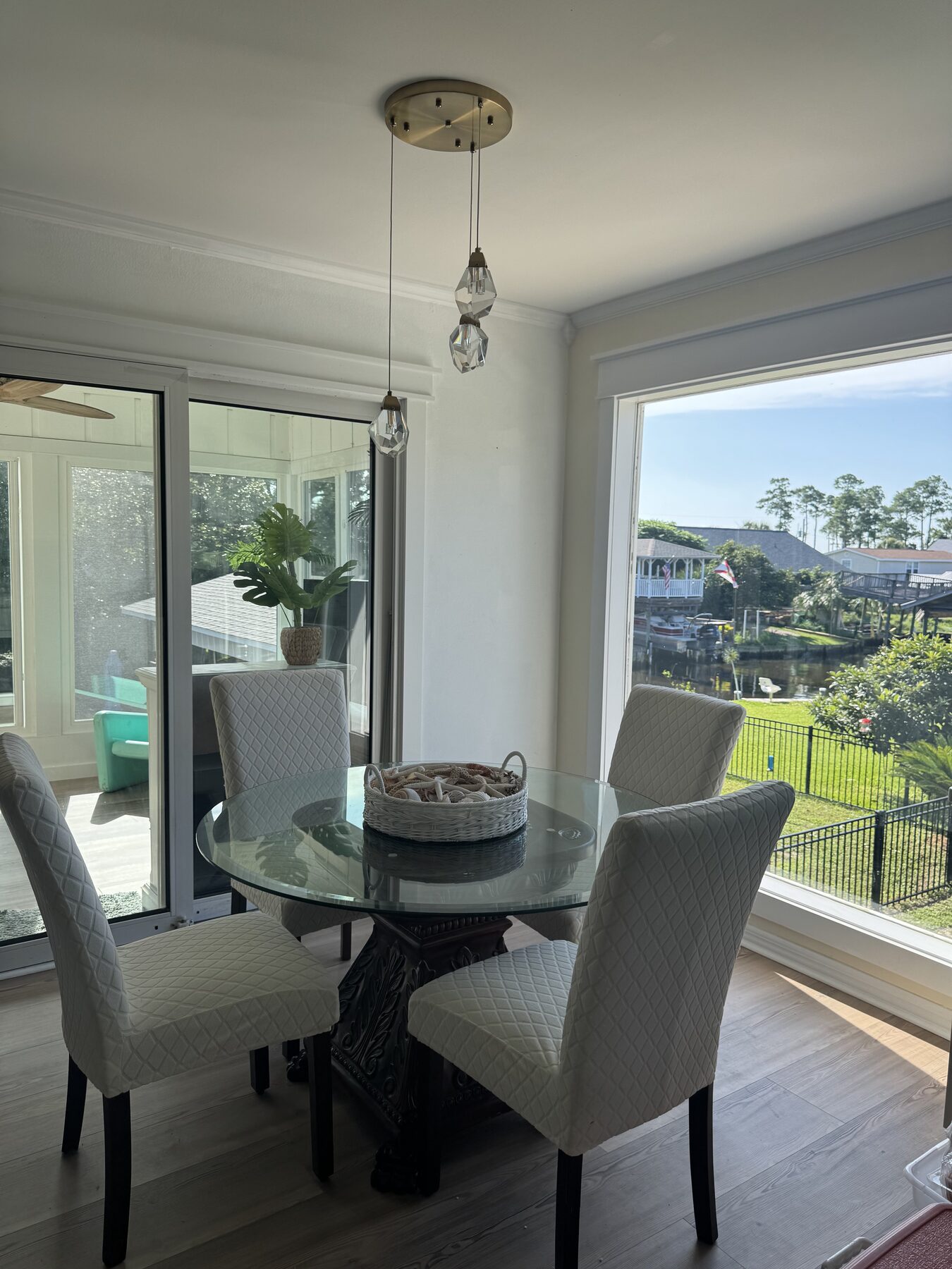 Round glass dining table with white upholstered chairs beside floor-to-ceiling windows overlooking the canal