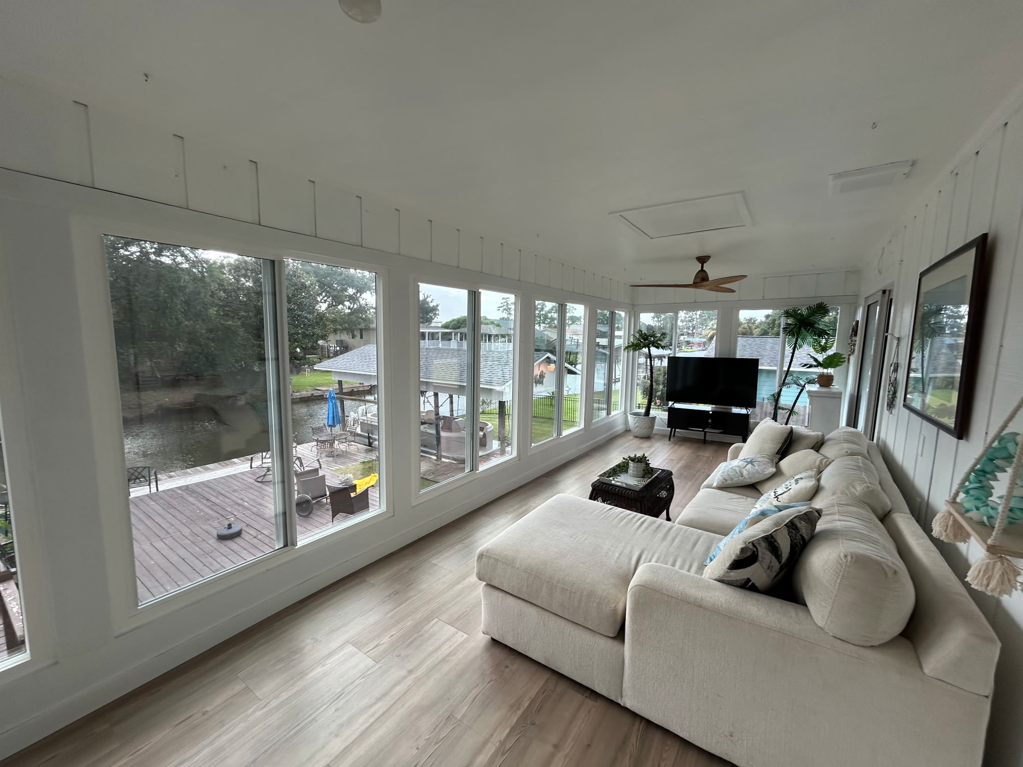 Sunlit Florida room with a large sectional sofa and a wall of windows looking out over the deck and canal