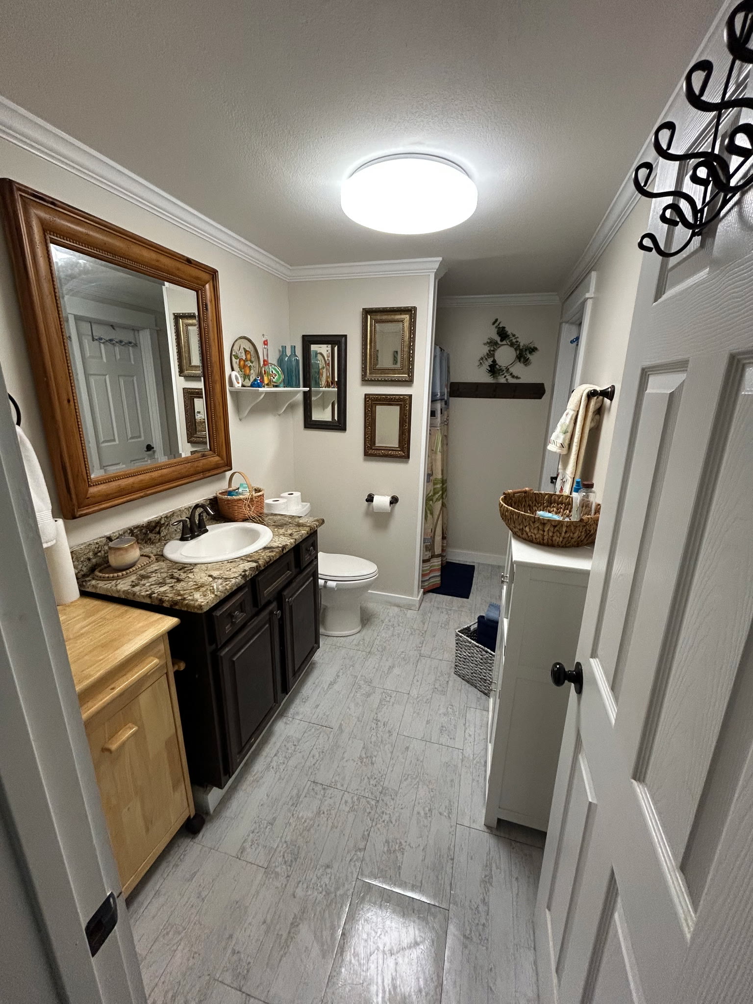 Guest bathroom with a granite vanity, framed wood mirror, tub-shower, and light tile floors