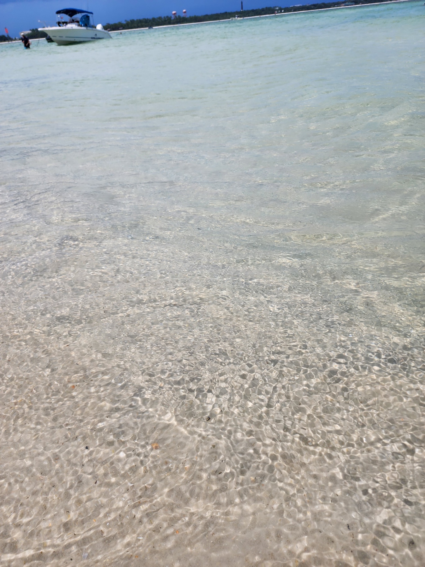 Crystal-clear shallow Gulf water with a boat anchored offshore near the Pensacola lighthouse