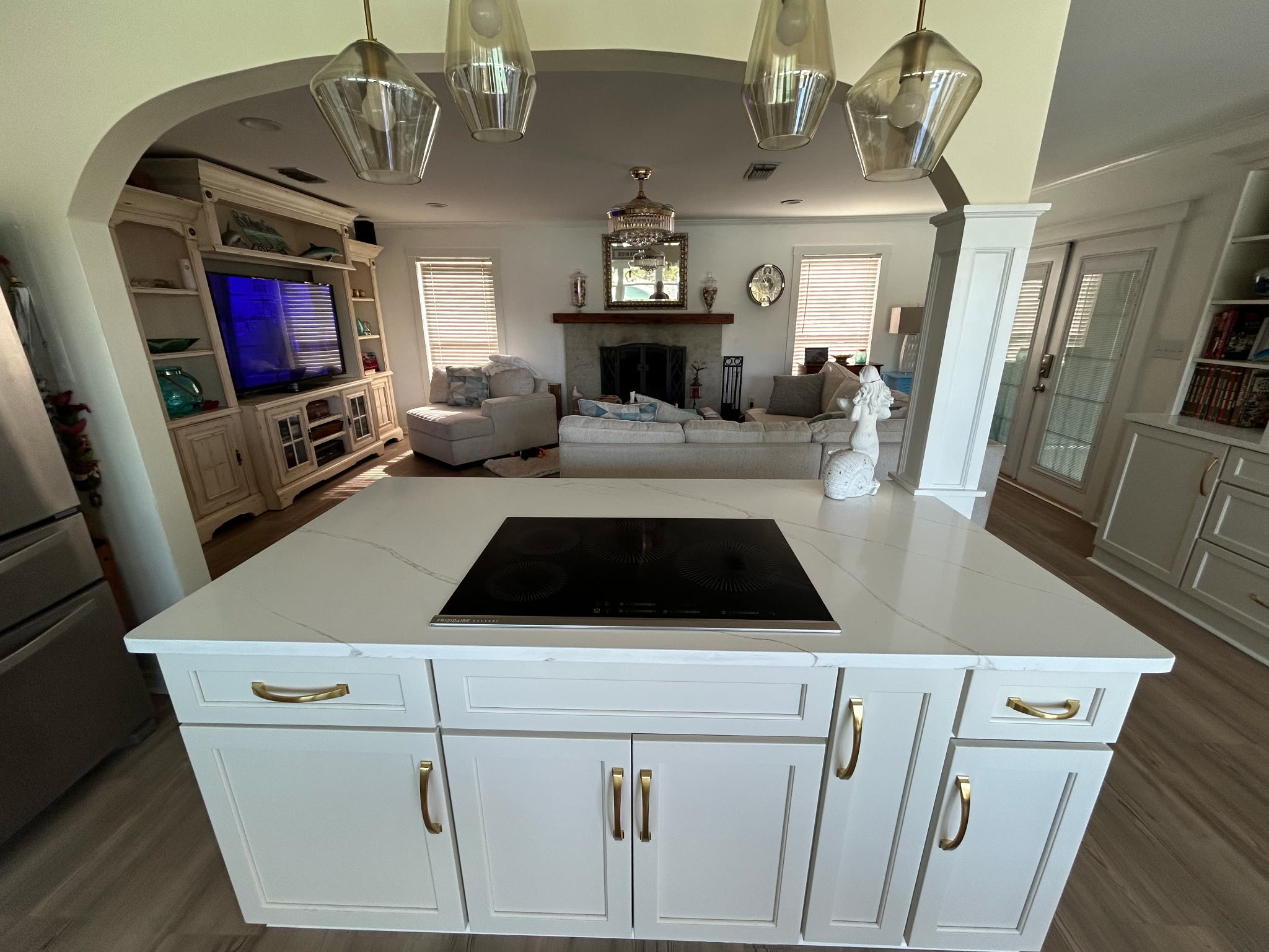 Kitchen island cooktop with pendant lights opening through an archway to the living room