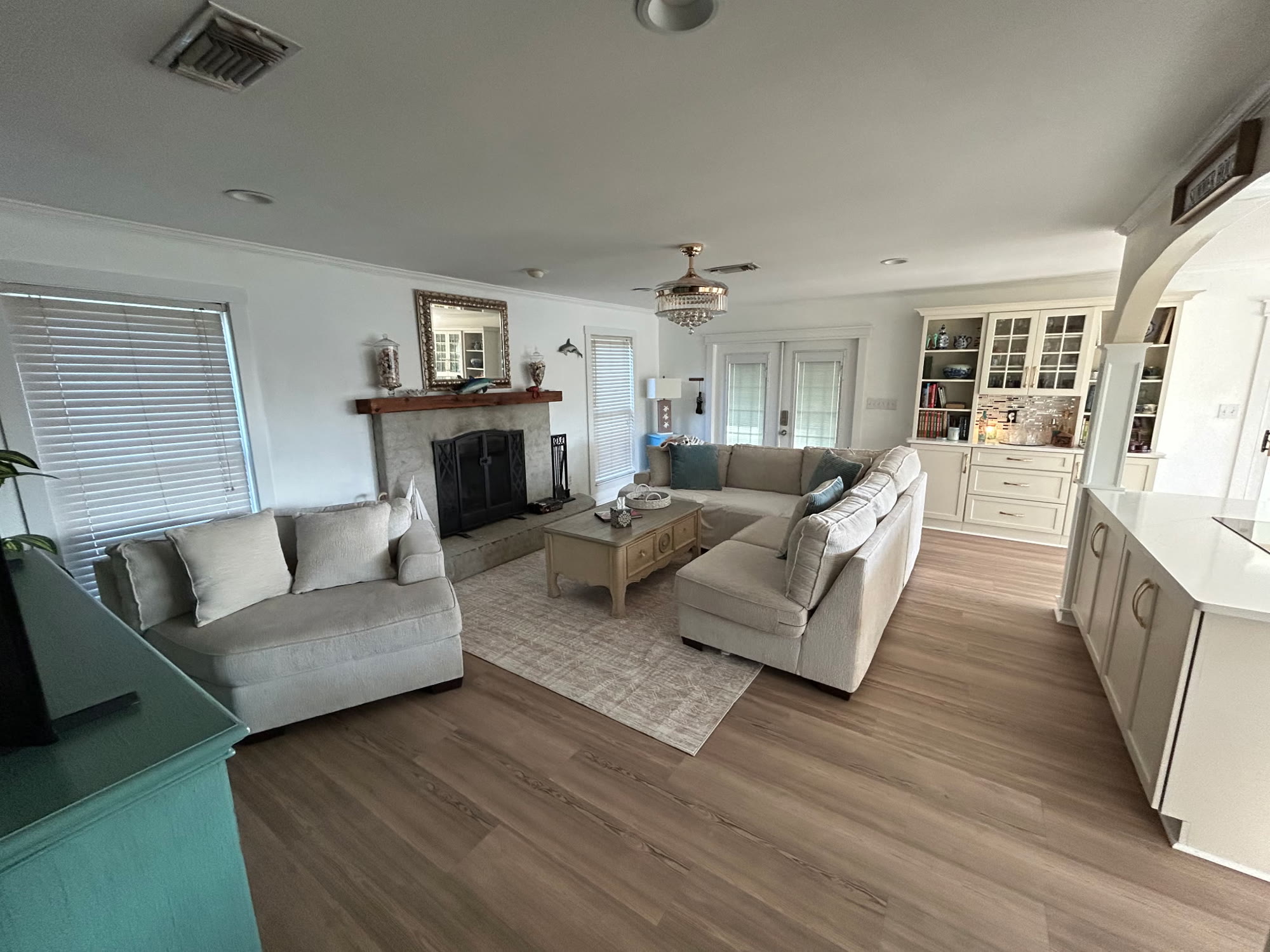 Bright coastal living room at White Lotus with two plush sofas, a stone fireplace, wood floors, and built-in china cabinets