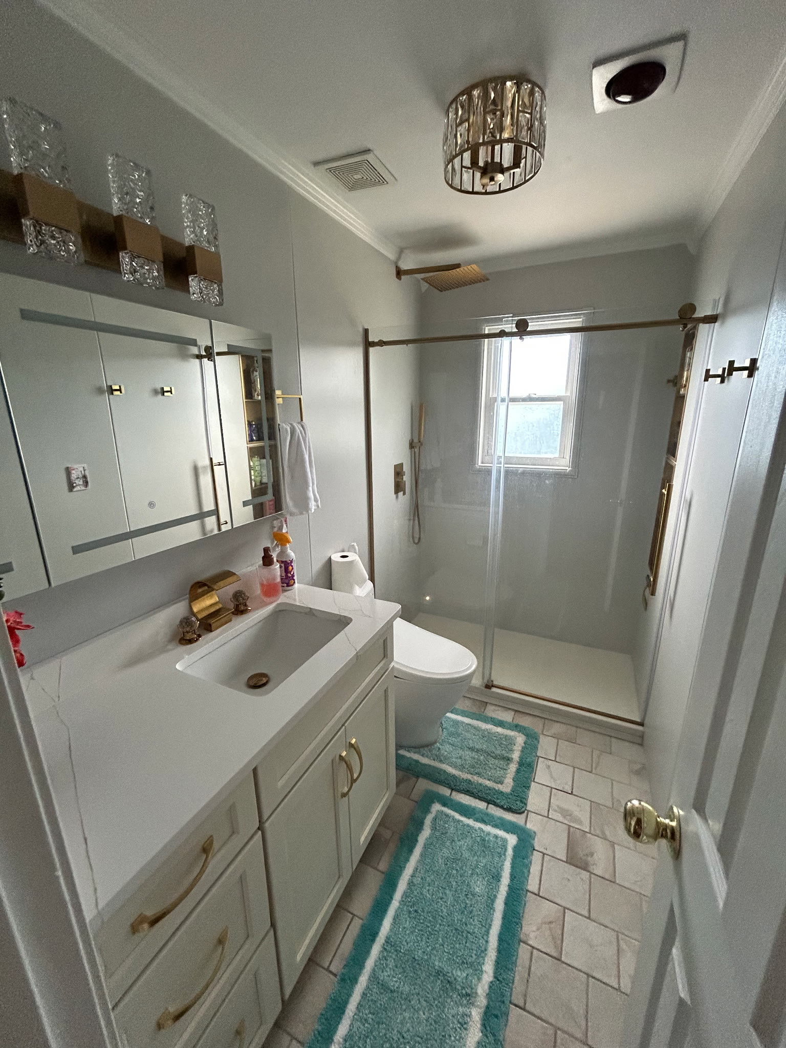 Updated master bathroom with a quartz vanity, gold fixtures, lighted mirror, and glass walk-in shower