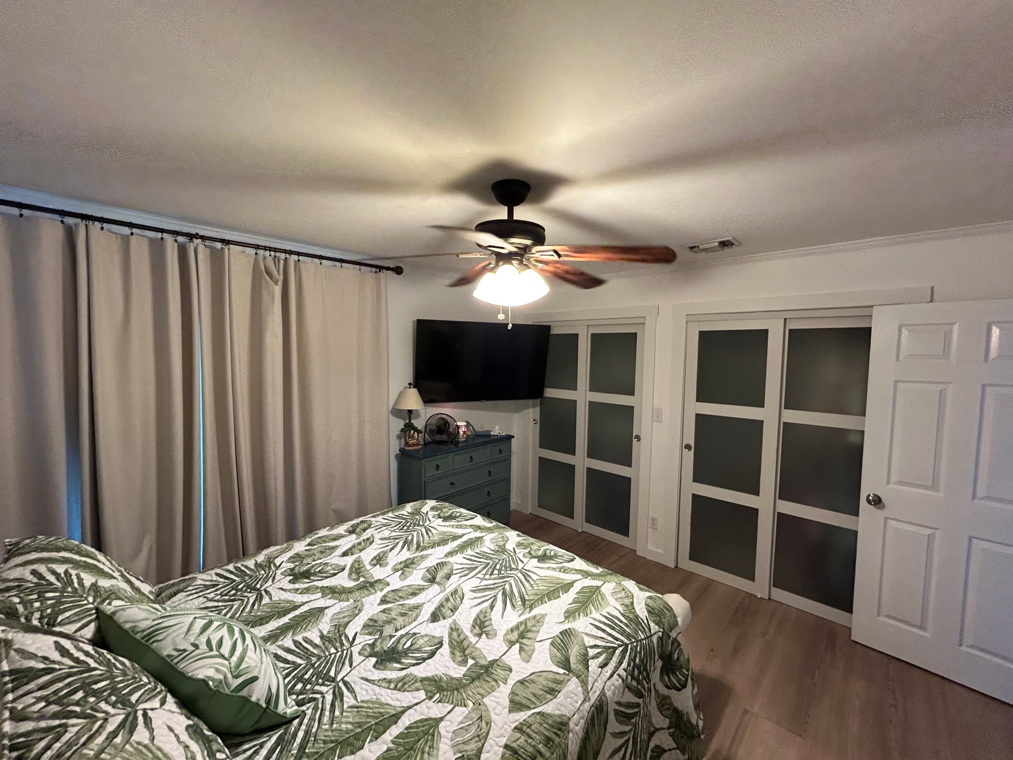 Second view of the master bedroom showing sliding closet doors, curtained windows, and ceiling fan